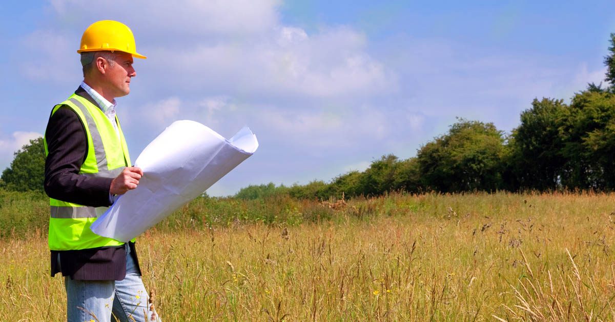 CONSTRUCTION Surveying rural lot with hard hat and blueprints